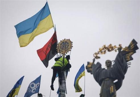 تظاهرات ضد دولتی مردم اوکراین همچنان در کی‌یف ادامه دارد. مردی از پایه فلزی (درخت کریسمس) بالا رفته تا نماد ملی این کشور را بیاویزد. CREDIT: REUTERS/GLEB GARANICH