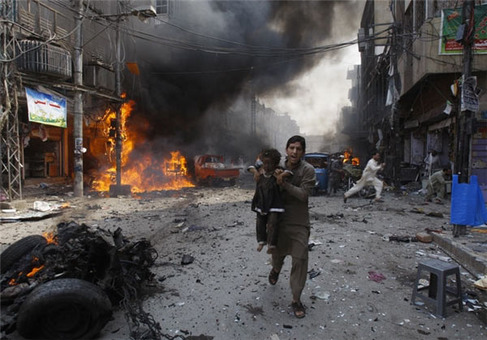 مردی در حال دور کردن کودک از محل انفجار یک بمب در پاکستان