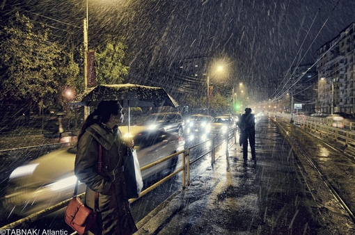 یک زن زیر باران شدید و رگبار ایستاده در ایستگاه تراموا در بخارست 