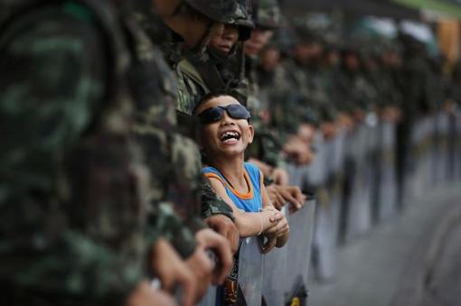 بازی پسر بچه در میان سربازانی که در خیابان‌های بانکوک، منع آمد و شد را برقرار کرده‌‌اند. 