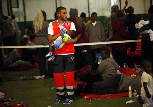 یک امدادگر صلیب سرخ اسپانیایی در حال کمک به تغذیه یک نوزاد مهاجر آفریقایی در کمپ مهاجرین