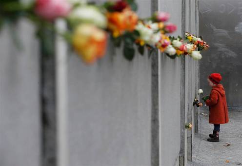 دختری به مناسبت بیست و پنجمین سالگرد فرو ریختن دیوار برلین، یک گل رز را در مکان یادبود آن در خیابان برناوه می‌گذارد./REUTERS
