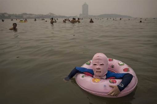 یک دختر چینی با ماسک و لباس مخصوص برای در امان ماندن از جلبکها و گزندگی حشرات و اشعه ماورابنفش خورشید در دریای زرد شنا می کند./Getty Images