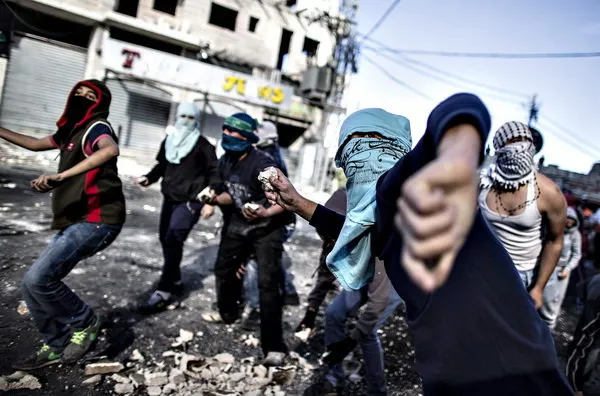 جوانان فلسطینی در یک ایست بازرسی بین کمپ آوارگان شوافات و قدس، در حال پرتاب سنگ به سمت نیروهای پلیس مرزی رژیم صهیونیستی هستند. /Reuters
