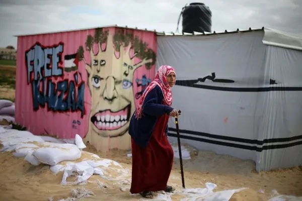 یک زن فلسطینی عصا به دست در اطراف اردوگاه موقت فلسطینیان راه می&zwnj;رود.

