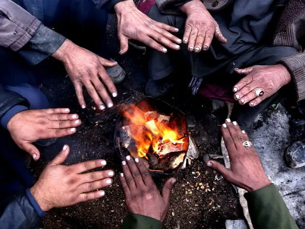 کارگران افغان در سرمای سخت پاییزی در شهر هرات دستان خود را دور آتش گرم می&zwnj;کنند. (EPA)

